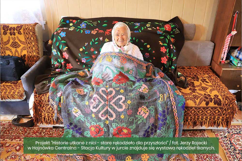 Projekt ,,Historie utkane z nici-stare rękodzieło dla przyszłości."Starsza kobieta otoczona tradycyjnymi tkaninami podlaskimi