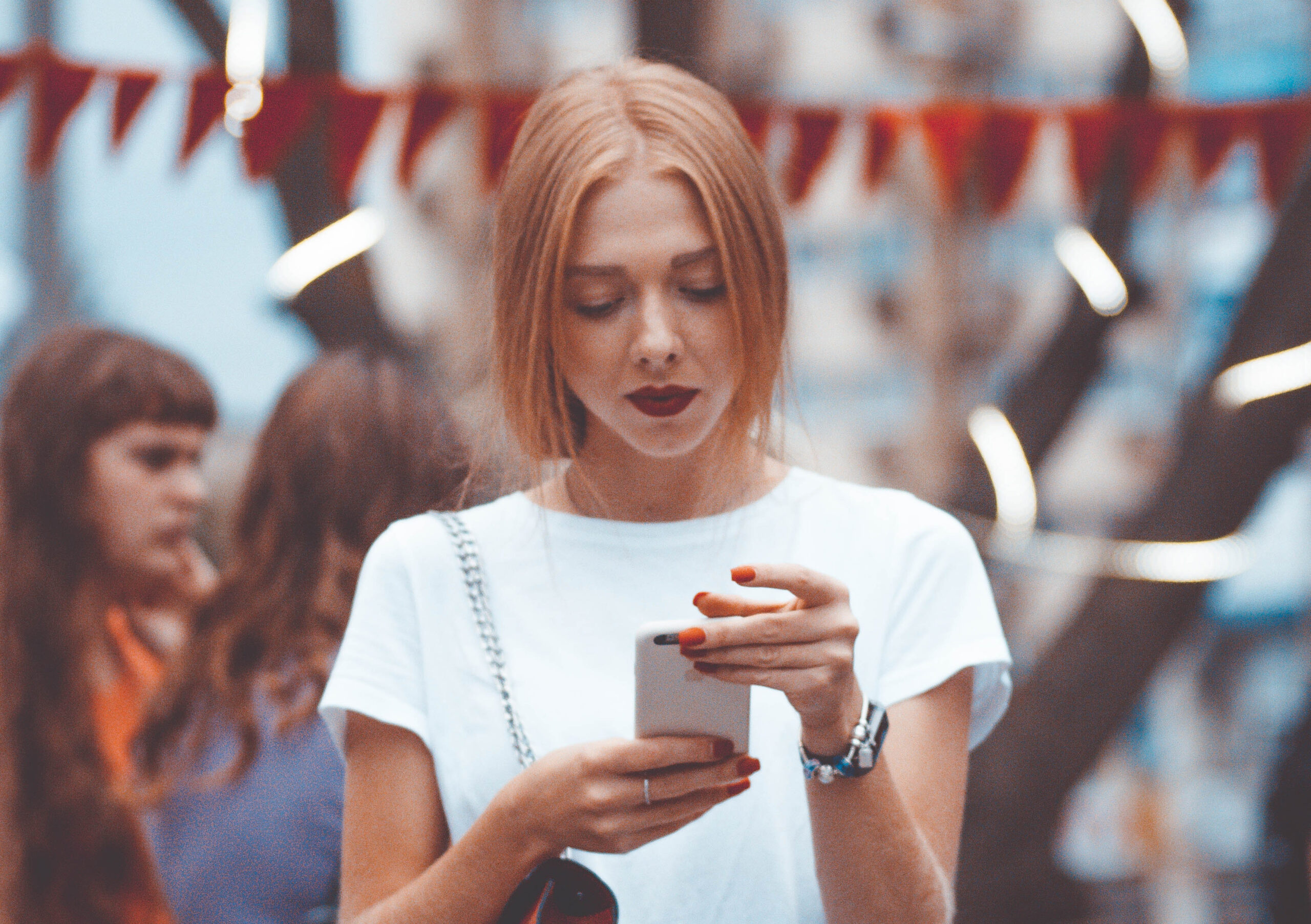 Młoda dziewczyna w białej bluzce spogląda w ekran telefonu.